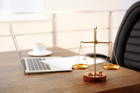 A desk with a laptop and the scales of justice on a criminal law attorneys desk.