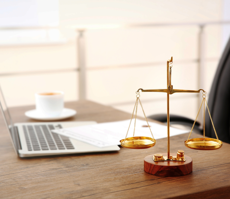 A desk with a laptop and the scales of justice on a criminal law attorneys desk.