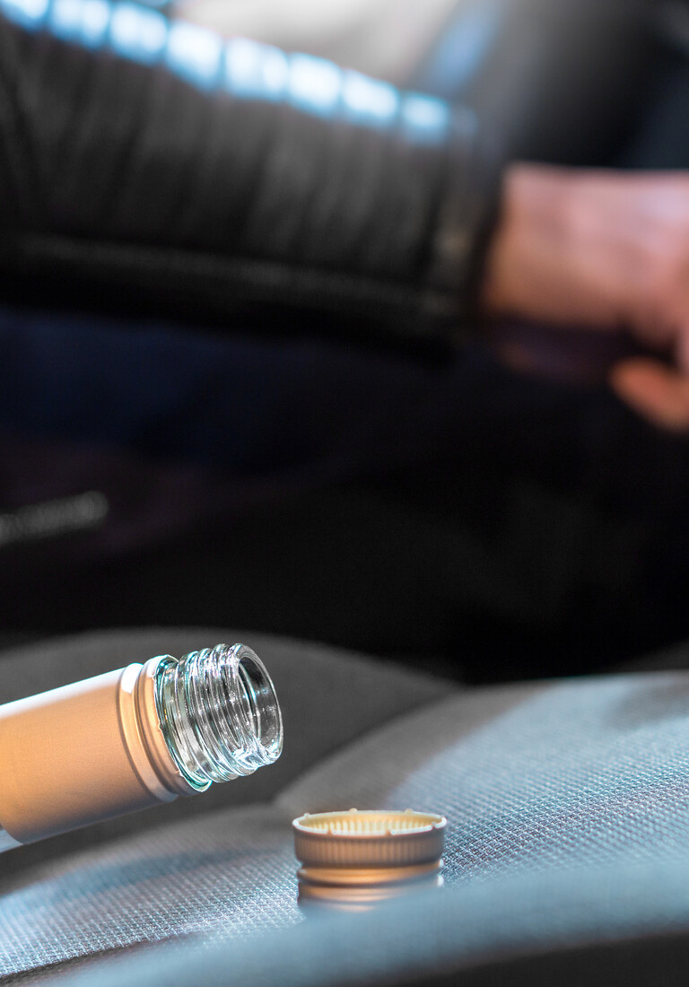 Young man driving car under the influence of alcohol. Hand on gear stick. Close up of empty bottle of wine on front seat. Traffic safety risk.