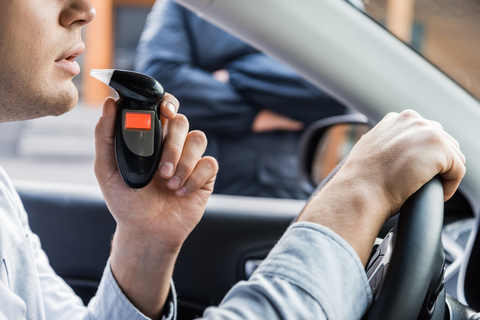 A man taking a breathalyzer test while sitting in his car.