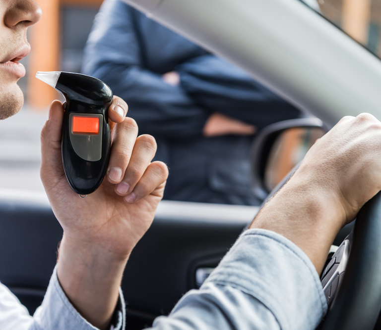 A man taking a breathalyzer test while sitting in his car.