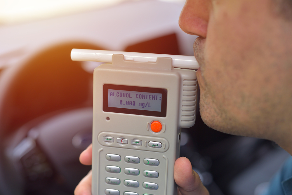 A man blowing into a breathalyzer device during a DUI stop.