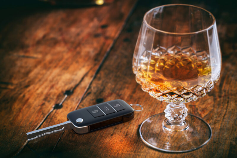 Glass of alcohol and car key sitting on a wood table representing a DUI. 
