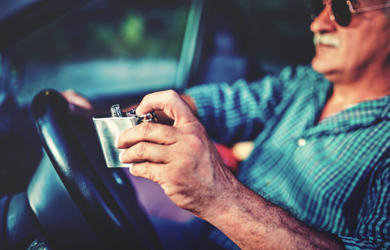 Elderly man drinking from a flask while driving. Our Johnson County DUI & DWI lawyers know how to fight for those arrested while driving while drunk.