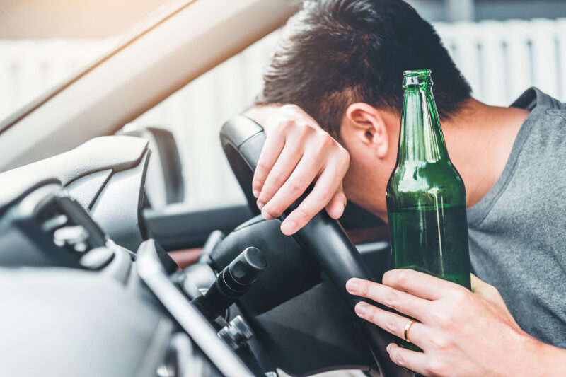 Young man holding beer bottle while lying drunk on the steering wheel. If you’ve been arrested while driving under the influence in Johnson County, contact a DUI & DWI lawyer now.