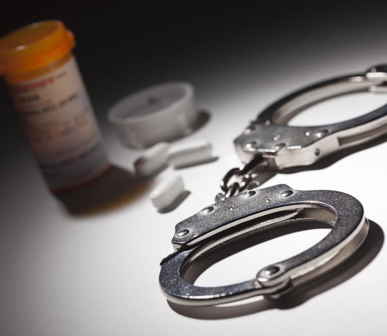 An open prescription pill container next to handcuffs on a table.
