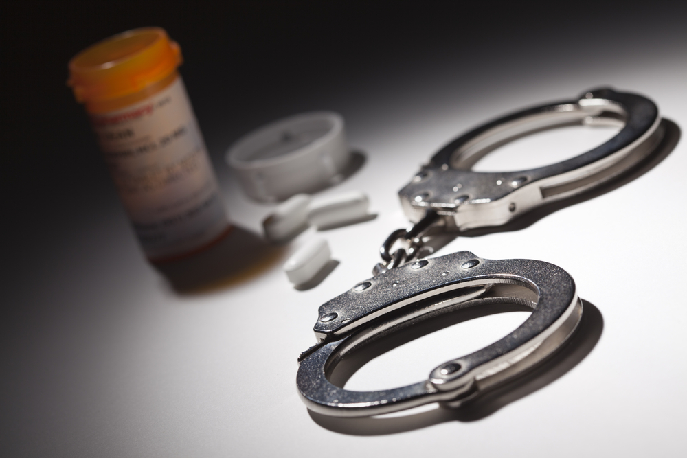 An open prescription pill container next to handcuffs on a table.