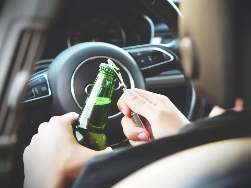 A driver sitting in the car and opening a beer bottle.