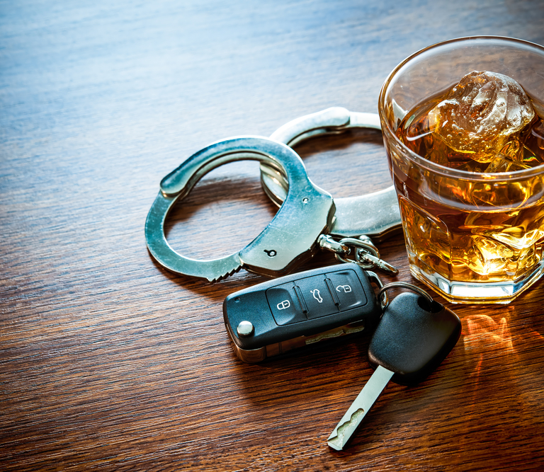 A cup with an alcoholic drink sitting next to handcuffs and car keys.