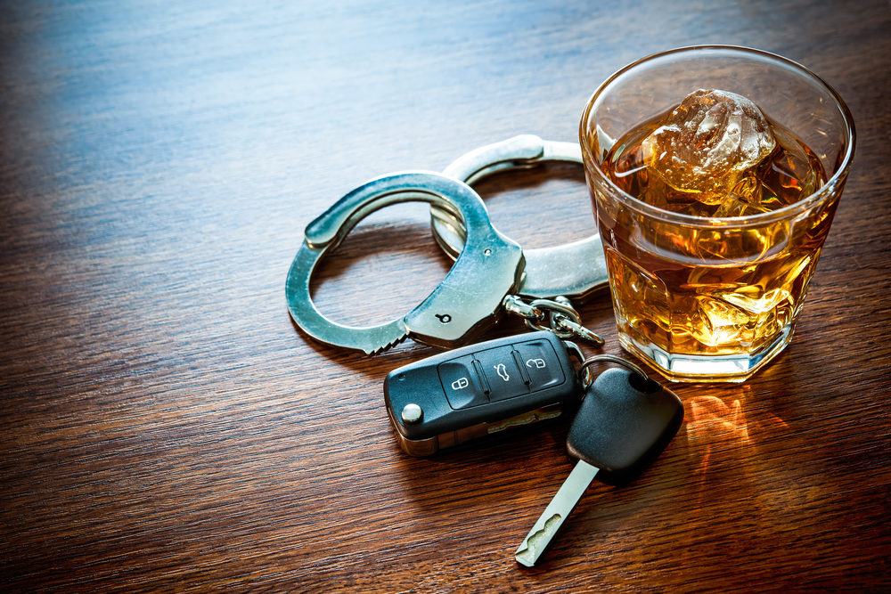 A cup with an alcoholic drink sitting next to handcuffs and car keys.
