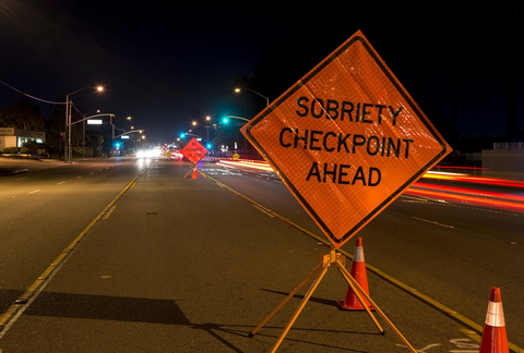 A street at night with cars going past a sobriety checkpoint.