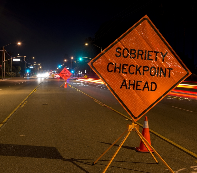A street at night with cars going past a sobriety checkpoint.