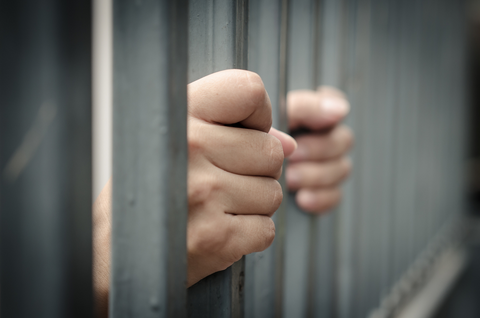 Hands grabbing onto jail cell bars.