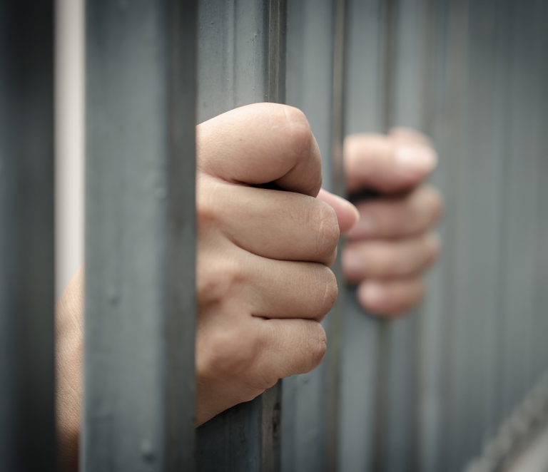 Hands grabbing onto jail cell bars.