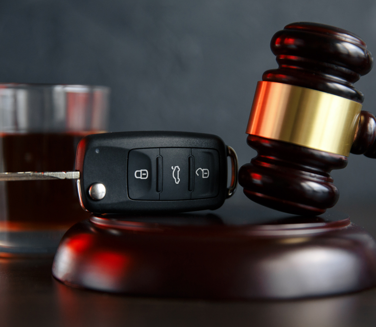 A car key and gavel with a drink in the background.