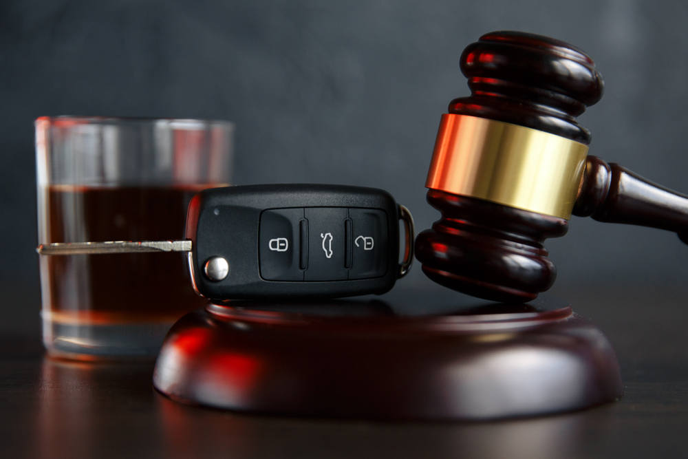 A car key and gavel with a drink in the background.