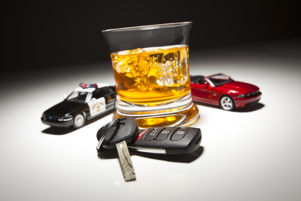 An image of a car keys, and an alcoholic drink, with a cop car and red car sitting next to it.