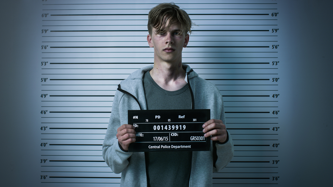 Teen boy posing for a mugshot in a dimly lit room. If your child has been charged with a misdemeanor or felony crime in Olathe or Overland Park, our criminal defense lawyers are ready to fight for you.